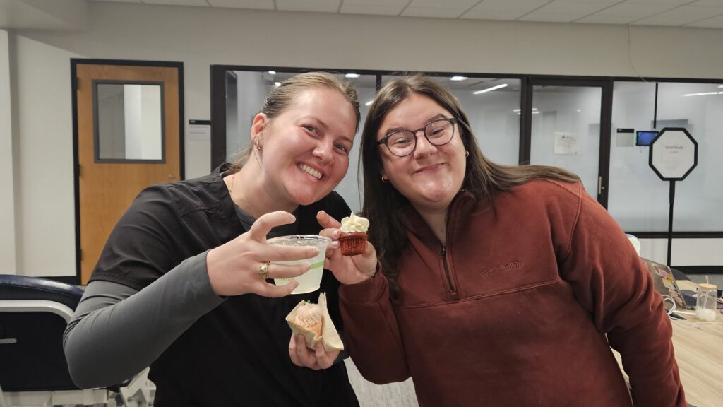 Two U N T H S C students smiling and posing with cupcakes and mocktails at Balcony Bash, Lewis Library 2025